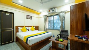Habitación de hotel con cama, escritorio, silla, unidad de aire acondicionado, ventana con cortinas y puerta.