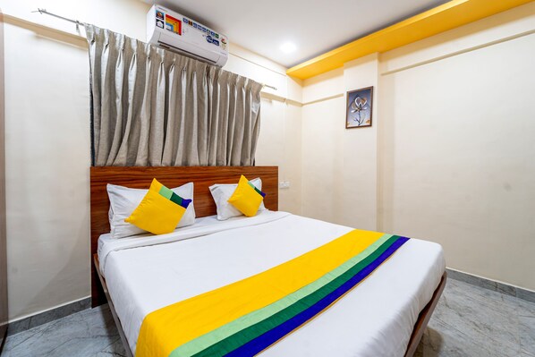 Una habitación de hotel con una cama, cortinas, un equipo de aire acondicionado y un cuadro en la pared.