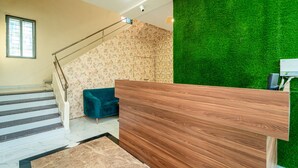 Una zona de recepción con un mostrador de madera, un sofá azul, una escalera con barandilla y una pared verde.