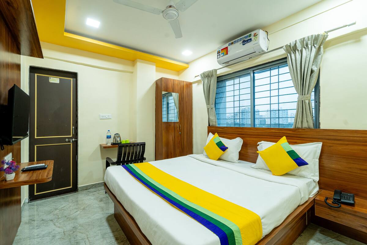 A hotel room with a bed, bedside table, and a window with curtains.