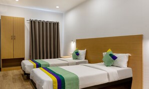 Two single beds with white bedding and colorful striped bedspreads, a wooden wardrobe, and a bedside table with a lamp.