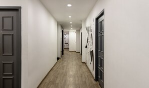 Un couloir doté d’un plancher en bois, de murs blancs et de portes de part et d’autre.