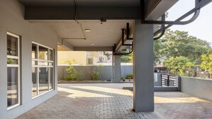 Um espaço ao ar livre coberto, com piso de azulejos, grandes janelas e plantas em vasos.