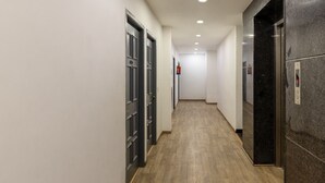 Um corredor com piso de madeira, portas escuras e elevador de mármore.