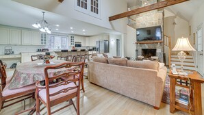 A spacious kitchen with white cabinets, a dining area with a table and chairs, a beige sofa, and a fireplace. - Peaceful Cavendish Retreat w/ Hot Tub & Fireplace! (Proctorsville)