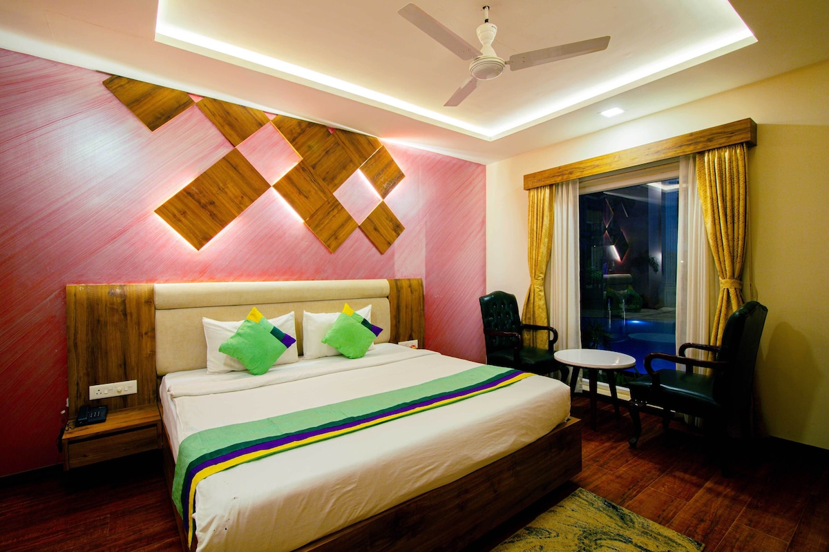 A hotel room with a bed, a ceiling fan, a window with curtains, and a small table with chairs.
