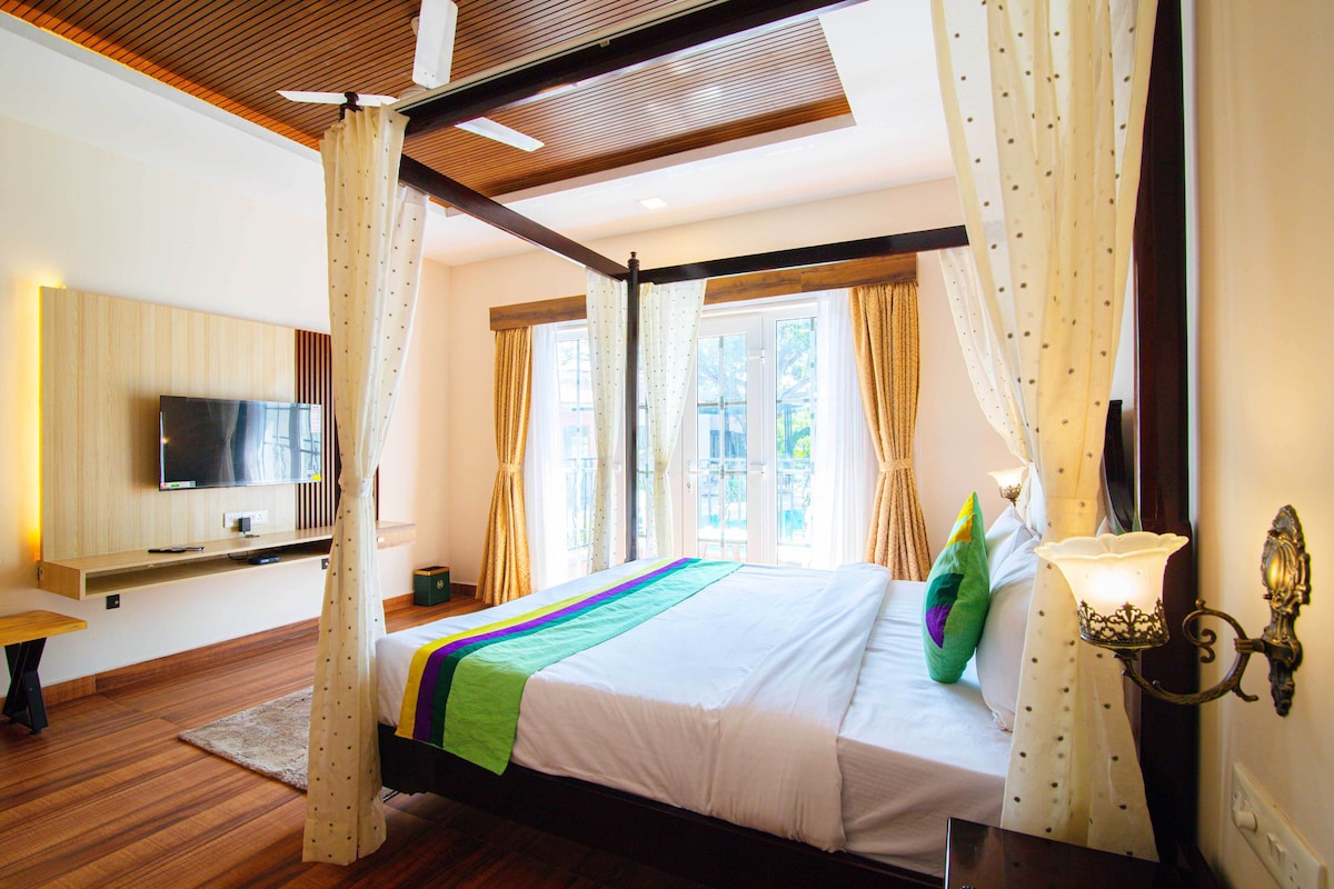 A bedroom with a bed, a TV, a bedside table, and a window with curtains.