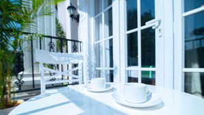 A white table with two white cups and saucers, a white chair, and a white railing. - Treebo Greenland Resort Patia with Swimming Pool (Bhubaneshwar)