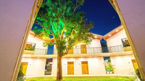 A building with a central tree illuminated by green lights, a courtyard with a grassy area, and a two-story structure with balconies and doors. - Treebo Greenland Resort Patia with Swimming Pool (Bhubaneshwar)