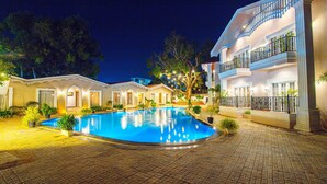 A swimming pool surrounded by a brick pathway, with a building featuring balconies and a poolside area. - Treebo Greenland Resort Patia with Swimming Pool (Bhubaneshwar)