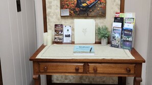 A wooden desk with a framed painting of a park bench and trees, a welcome booklet, and brochures on the side.