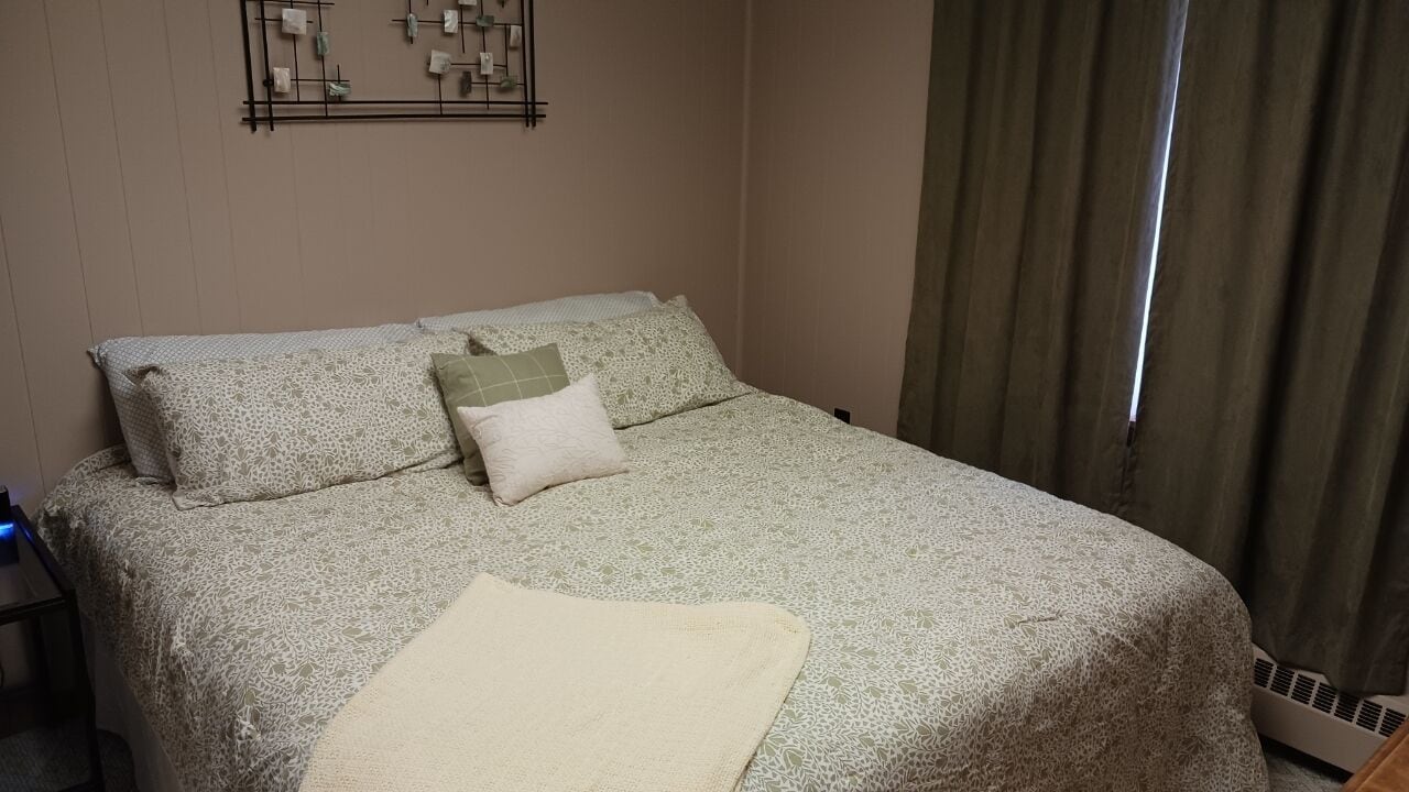 A neatly made bed with patterned bedding and pillows, a bedside table with a lamp, and a wall-mounted light fixture.