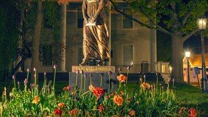 A statue of Mary Wells Morris in a garden with tulips and trees.