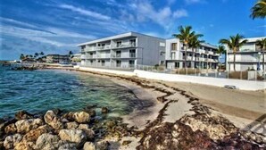A beachfront hotel with multiple balconies, a clear view of the ocean, and a rocky shoreline.