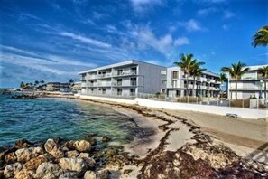 A beachfront hotel with multiple balconies, a clear view of the ocean, and a rocky shoreline.