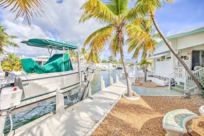 A boat docked at a marina with a palm tree and a building in the background.