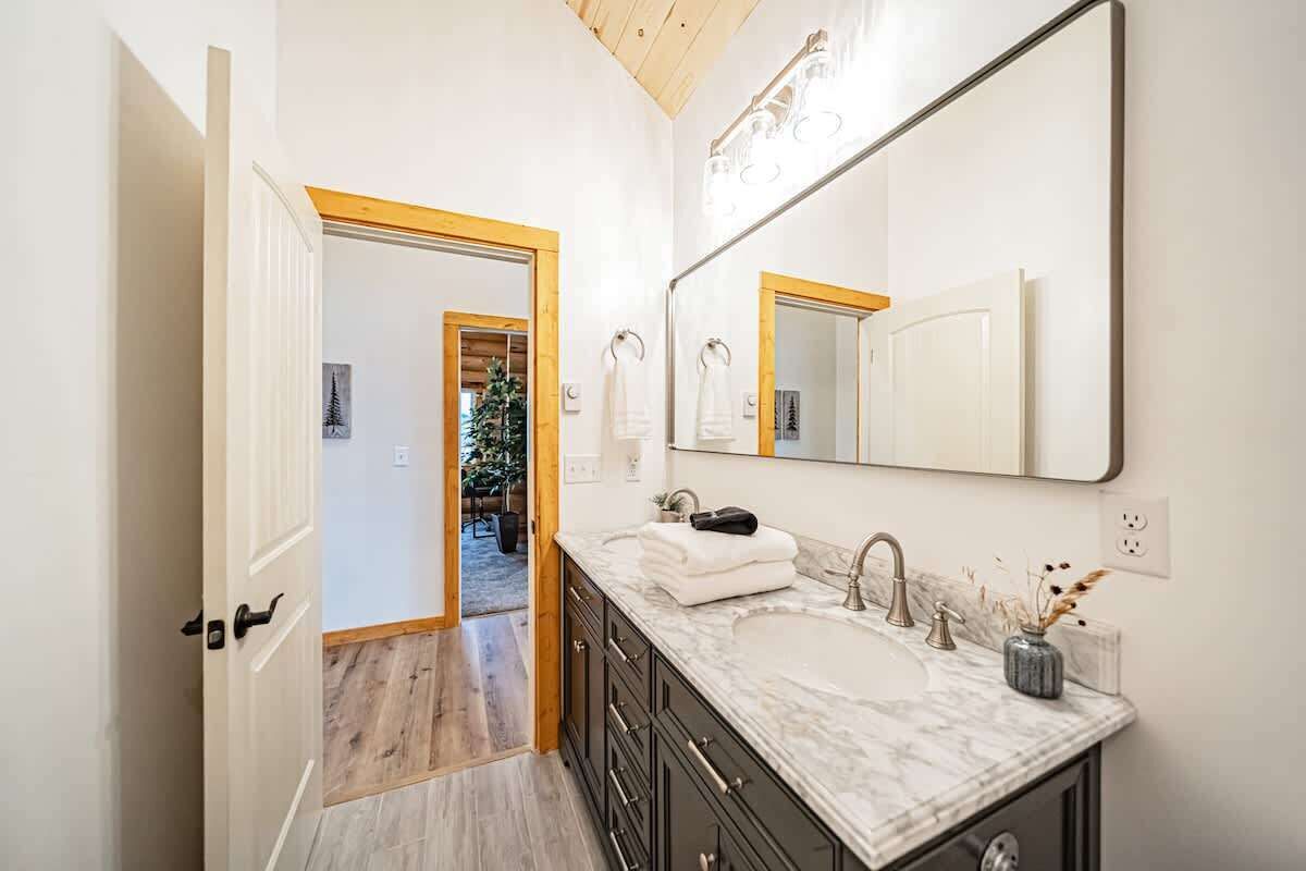 A bathroom with a large mirror, two sinks, and a wooden floor.