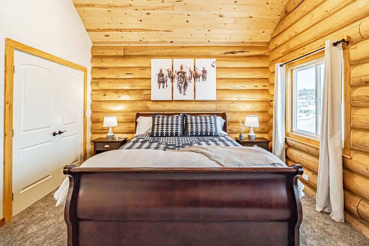 A wooden cabin bedroom with a bed, two bedside tables, and a window with curtains.