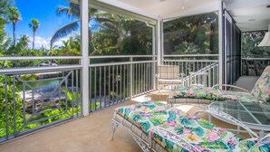 Ein Balkon mit Glasgeländer, Deckenventilator und Blick auf Pool und Grünflächen.