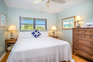 A bedroom with a bed, two bedside tables with lamps, a dresser, a window with blinds, and a ceiling fan.