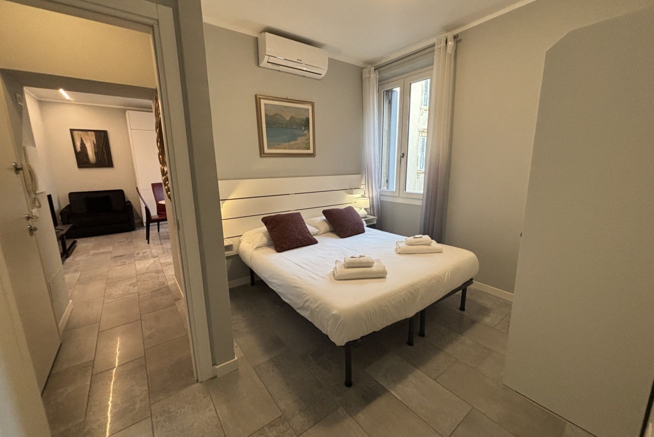 A hotel room with a bed, a painting on the wall, and a window with curtains.