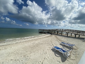 A beach with a wooden pier extending into the water, clear skies, and footprints in the sand. - Salty Breezes Condo 2bed 2bath second floor with elevator, pool & ocean front! (Key Colony Beach)