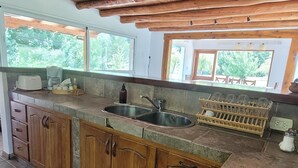Une cuisine avec des meubles en bois, une cuisinière à gaz, un évier et une fenêtre donnant sur un espace verdoyant.