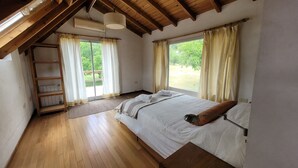 Une chambre avec un plancher en bois, un lit avec une literie blanche, une échelle en bois et une fenêtre avec des rideaux.