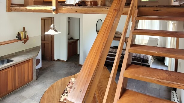 Un espace de vie de style loft avec un escalier en bois, un coin cuisine et un lit en mezzanine.