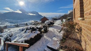 A wooden cabin with a snow-covered pathway leading to it, surrounded by mountains and a clear sky.
