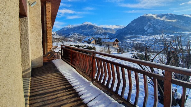 A balcony with a wooden railing overlooking a snowy mountain landscape.