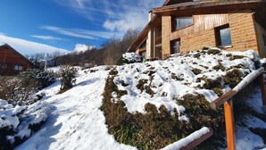 A modern wooden house with a sloped roof, large windows, and a snow-covered landscape.