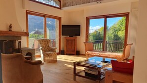 A spacious living room with a fireplace, comfortable seating, a television, and large windows offering a view of the outdoors.