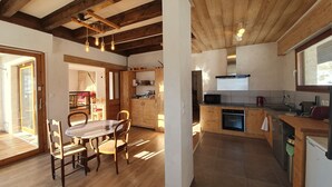 A modern kitchen with wooden beams, a dining area with a table and chairs, and a view of the outside.
