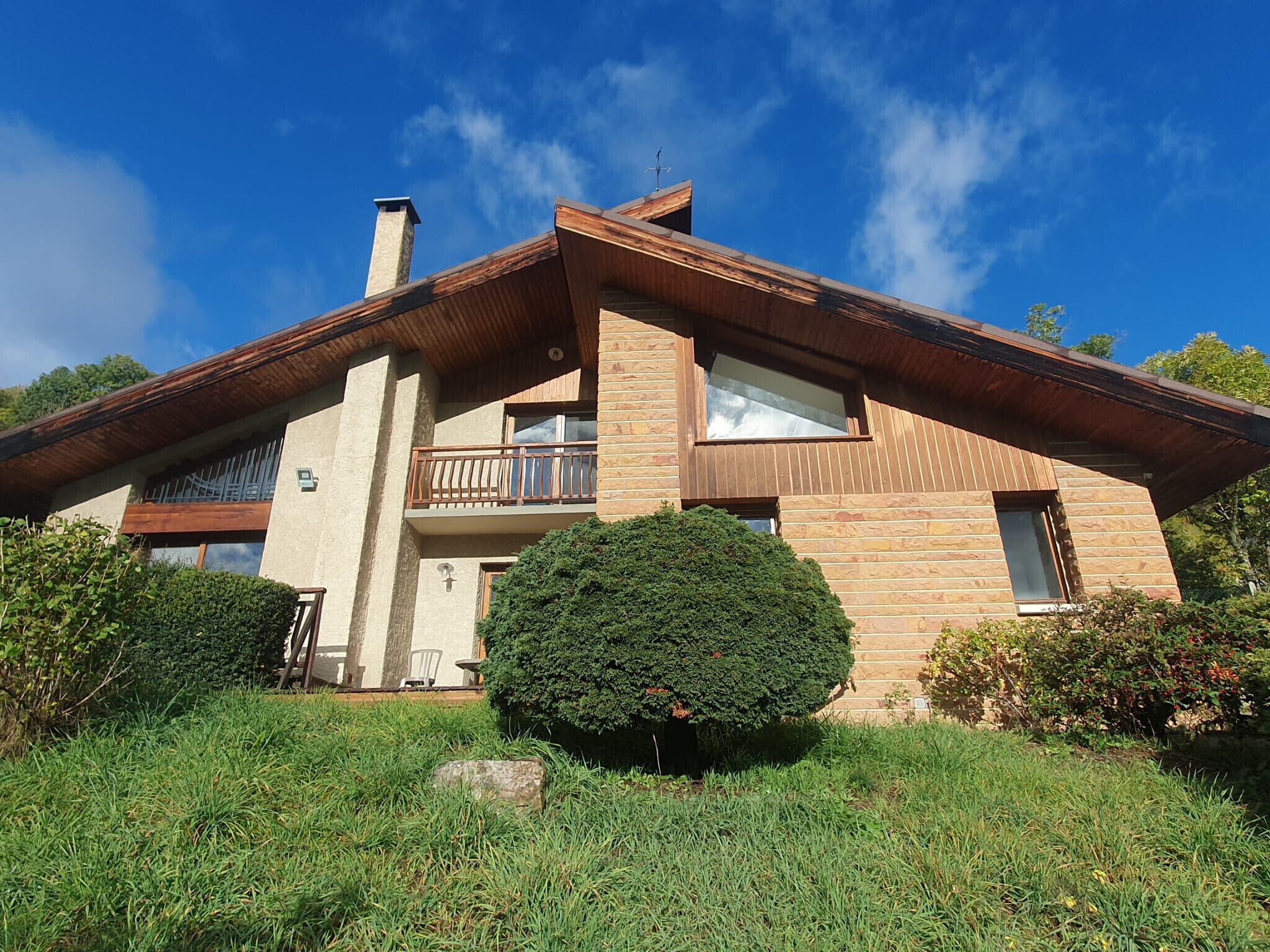 Una casa moderna de dos pisos con fachada de madera, un balcón y un césped cuidado.