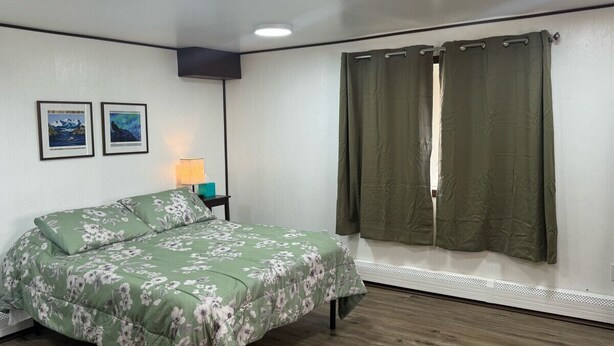 A bedroom with a bed, a nightstand, a lamp, two framed pictures, and a window with curtains. - Clean and Quiet Studio Apartment C (Nome)