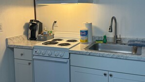 A compact kitchen with a white stove, a sink, and a coffee maker. - Clean and Quiet Studio Apartment C (Nome)