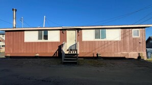 A single-story building with a brown exterior, a central door, and a small set of stairs leading to the entrance. - Clean and Quiet Studio Apartment C (Nome)