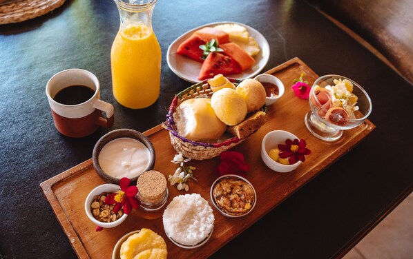 A wooden tray with breakfast items including bread, rice, and a bottle of orange juice.