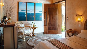 A bedroom with a large window, a wooden door, a wicker chair, a bedside table, and a bed with a quilted blanket. - Hotel Pousada Rancho das Dunas (Santo Amaro do Maranhão)