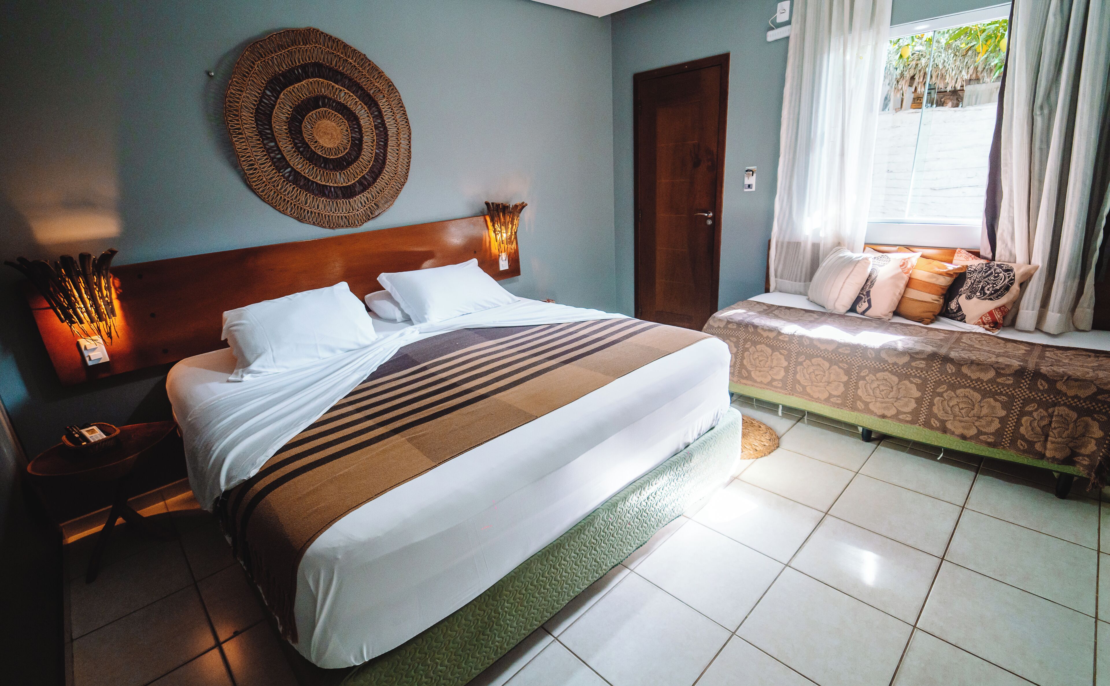 A hotel room with a large bed, a smaller bed, a wall-mounted circular decorative item, and a nightstand with a phone and a lamp.