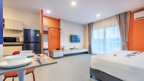A modern hotel room with a bed, a dining area with a table and chairs, a microwave, a refrigerator, and a TV. - PLAAI Plus Hotel Bowin (Pluak Daeng)