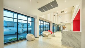 A modern lobby with large windows, a reception desk, and comfortable seating areas. - PLAAI Plus Hotel Bowin (Pluak Daeng)