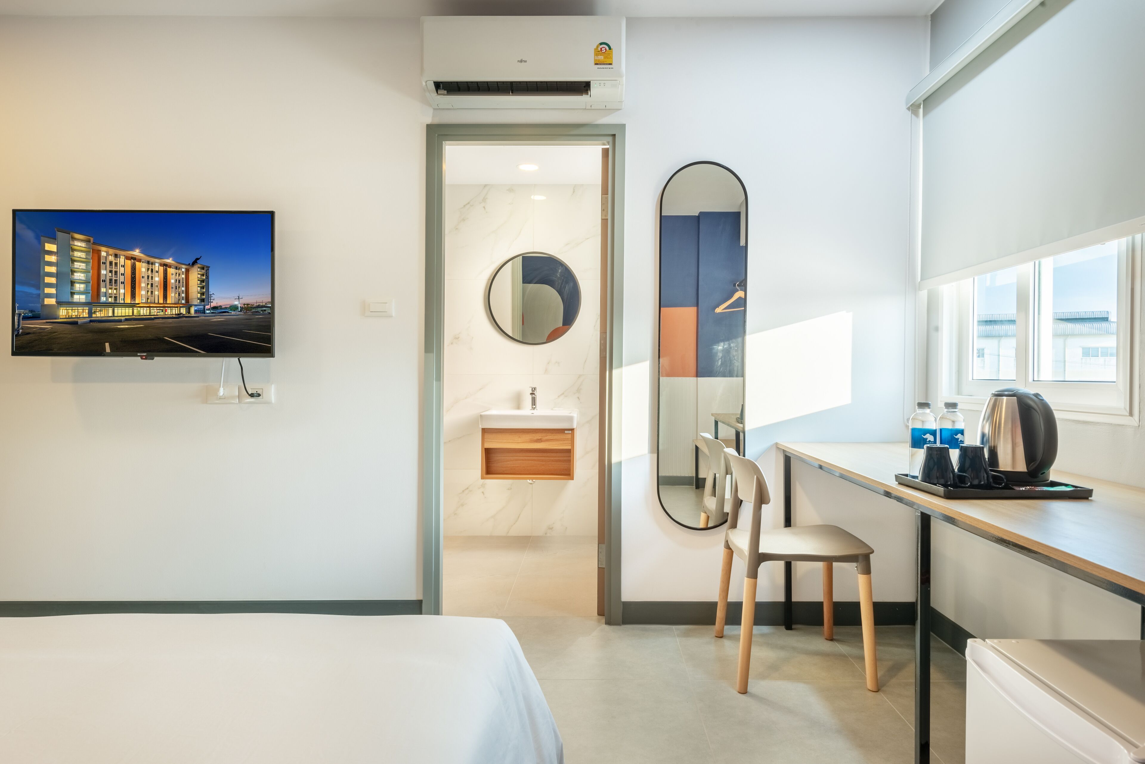 A hotel room with a bed, a desk with a chair, a mirror, a sink, and a window.