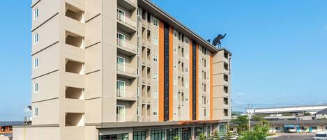 Un hotel de varios pisos con balcones, un estacionamiento y una estatua en la azotea.
