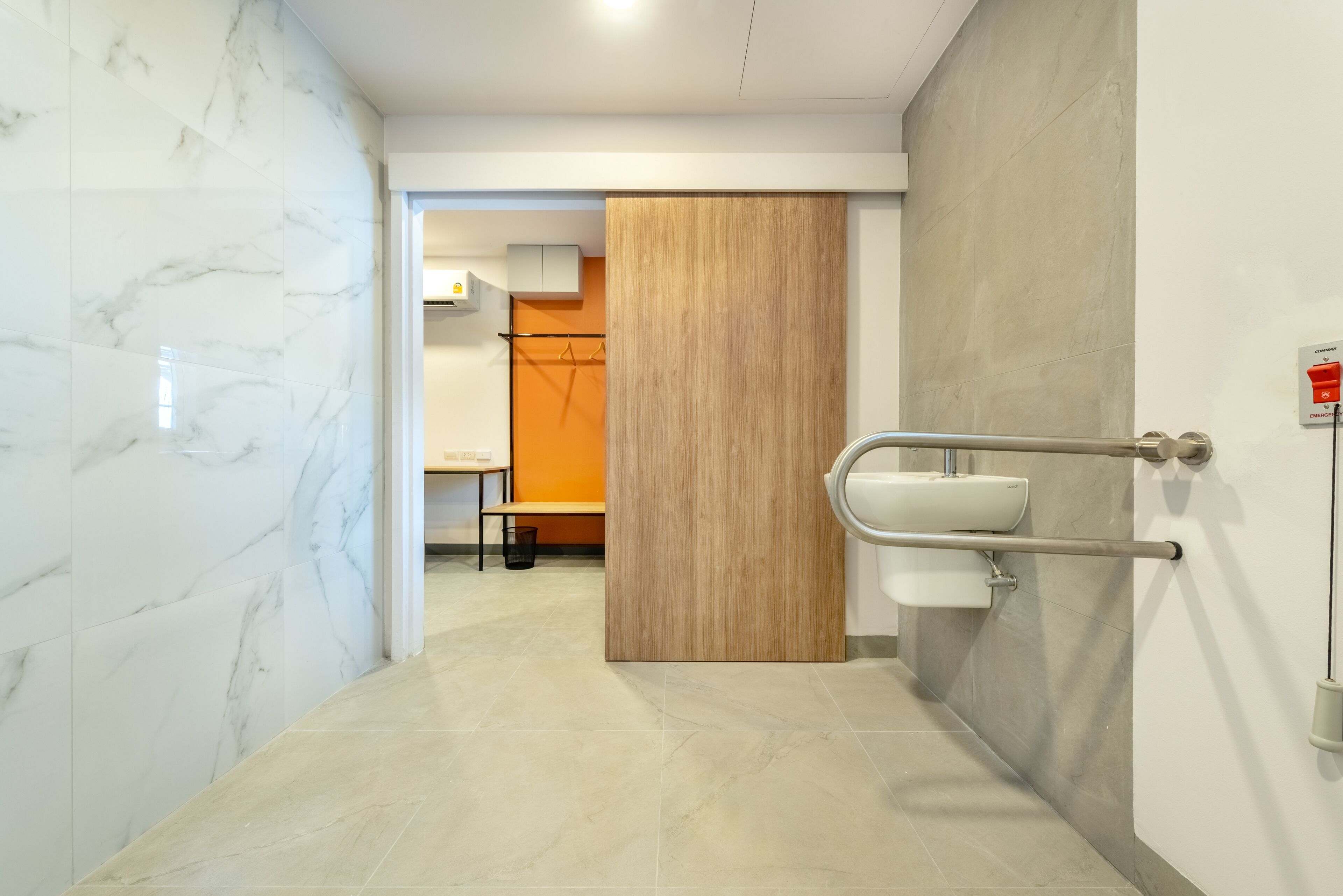 A modern bathroom with marble walls, a wooden panel, and a sink with a handrail.