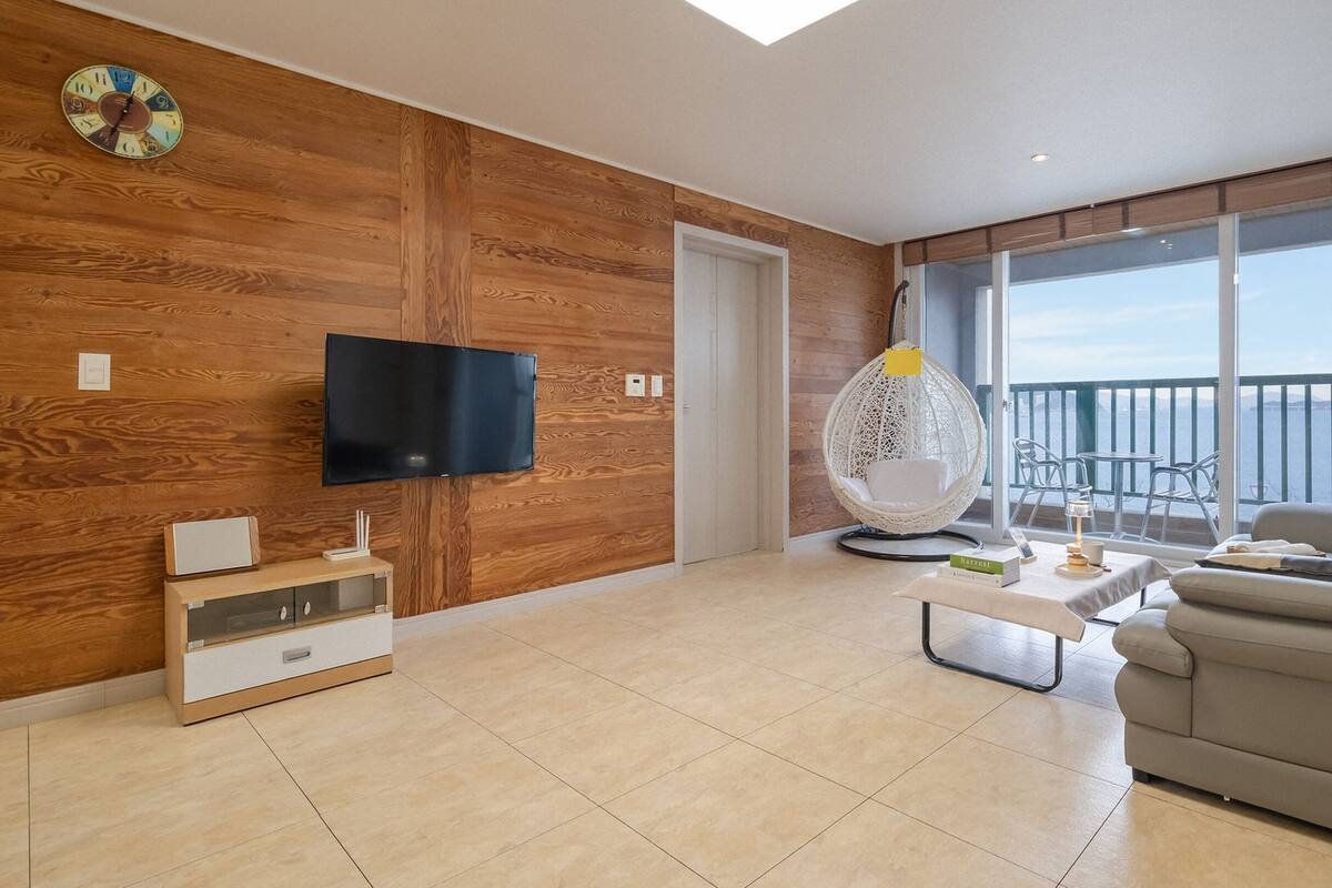 A modern living room with a flat-screen TV, a white sofa, a hanging chair, and a balcony with a view.