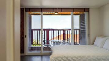 Una camera d'albergo con un letto, un balcone con tavolo e sedie, e vista sulla spiaggia.
