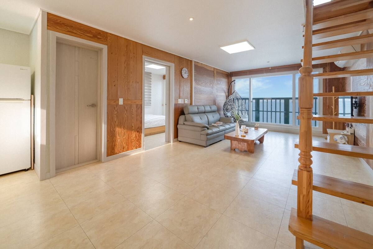 A spacious living area with a modern kitchen, a sofa, a coffee table, and a wooden staircase.