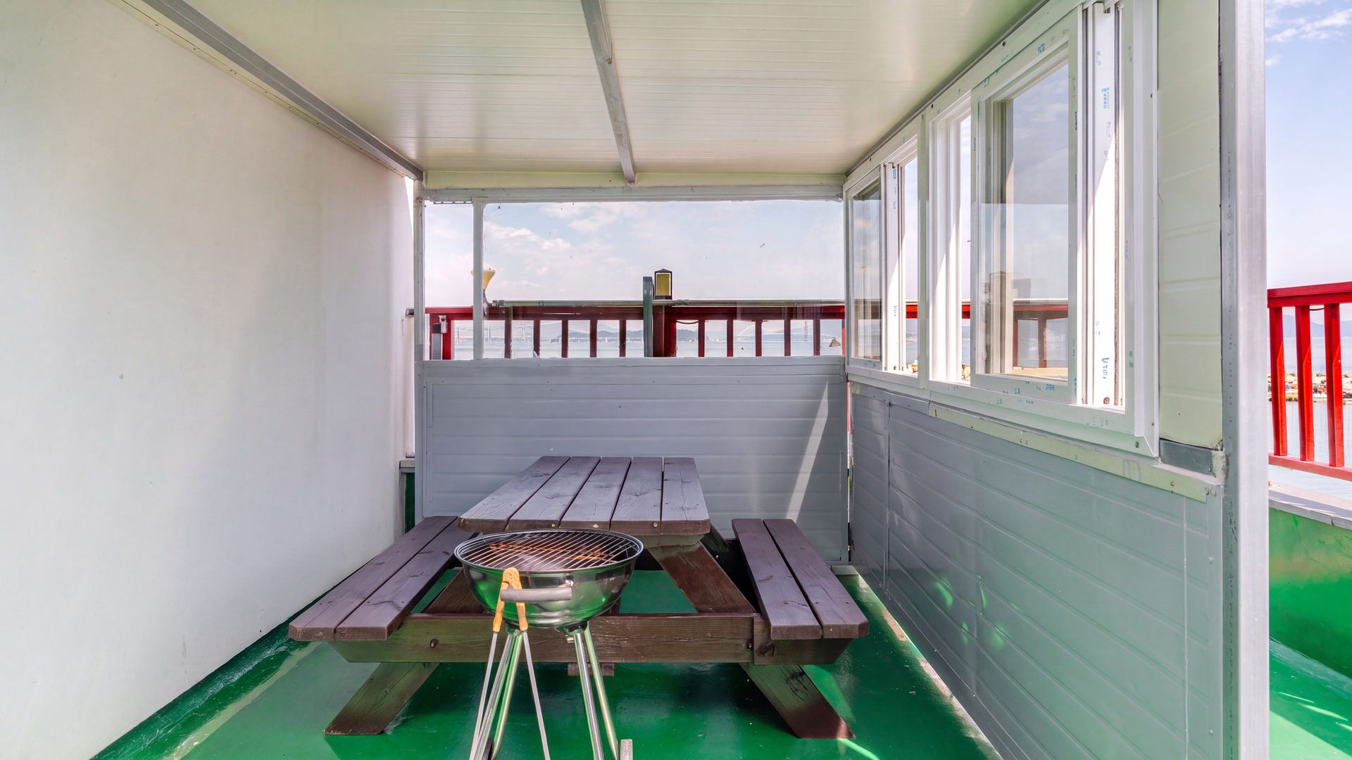 A covered outdoor area with a picnic table and grill, a railing, and a view of the water.